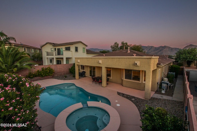 pool at dusk featuring a patio, a mountain view, and an in ground hot tub