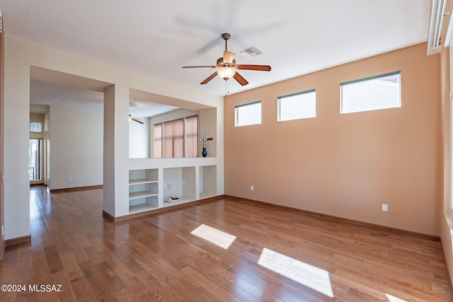 unfurnished room featuring a ceiling fan, visible vents, built in shelves, and wood finished floors