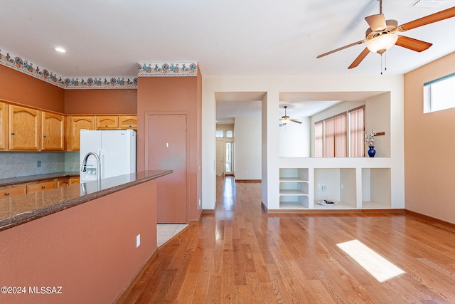 kitchen with tasteful backsplash, white fridge with ice dispenser, light wood-type flooring, dark stone countertops, and built in shelves