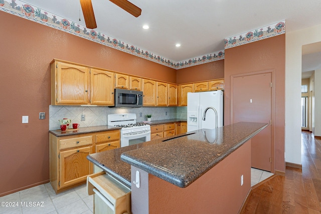 kitchen featuring white appliances, a kitchen island, ceiling fan, dark stone counters, and light hardwood / wood-style flooring