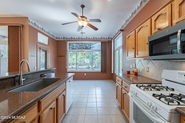 kitchen with tasteful backsplash, dark stone countertops, light tile patterned flooring, sink, and white appliances