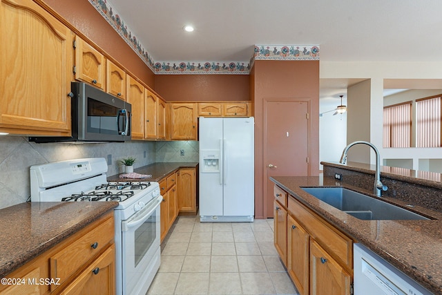 kitchen featuring dark stone counters, sink, light tile patterned floors, white appliances, and ceiling fan