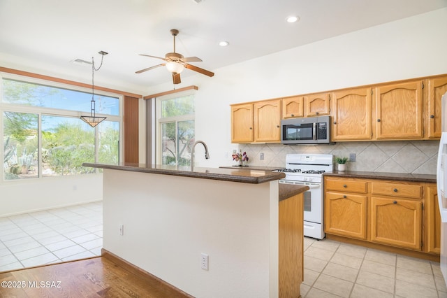 kitchen with decorative backsplash, pendant lighting, ceiling fan, white range with gas stovetop, and stainless steel microwave