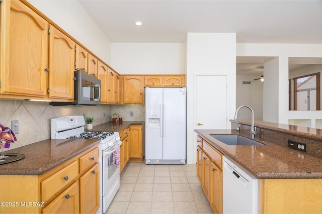 kitchen featuring light tile patterned flooring, a sink, white appliances, dark stone counters, and decorative backsplash