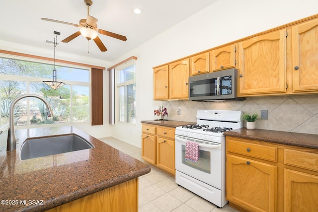 kitchen featuring a sink, dark stone countertops, stainless steel microwave, white gas stove, and decorative backsplash