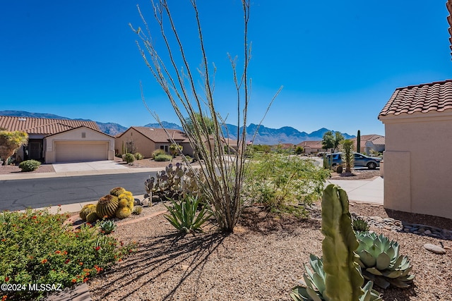 view of yard featuring an attached garage, driveway, a residential view, and a mountain view