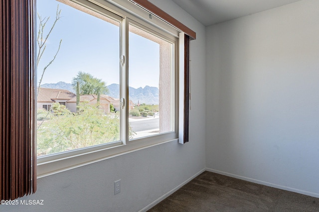 spare room with a mountain view, a wealth of natural light, and dark colored carpet
