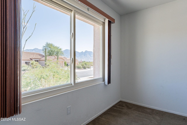 unfurnished room featuring dark colored carpet, a mountain view, and baseboards