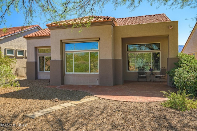 rear view of property featuring fence, stucco siding, a patio area, and a tile roof