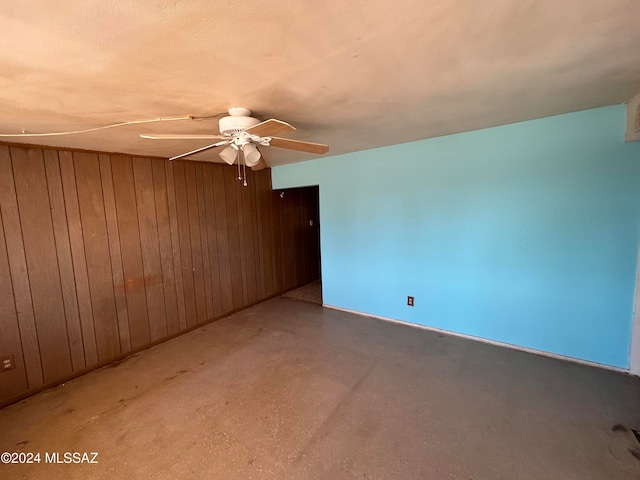 unfurnished room featuring wooden walls, ceiling fan, and concrete floors