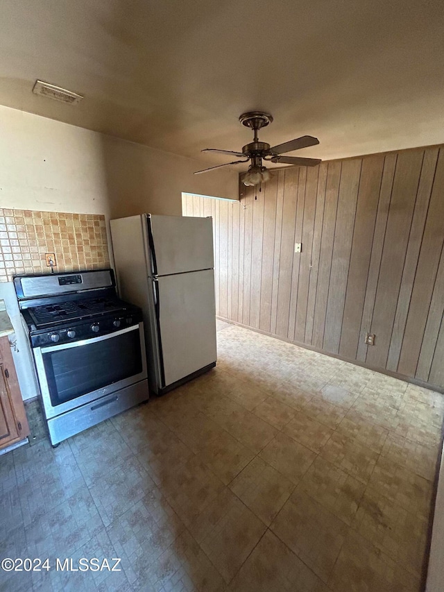 kitchen with wood walls, stainless steel range with gas stovetop, white fridge, and decorative backsplash