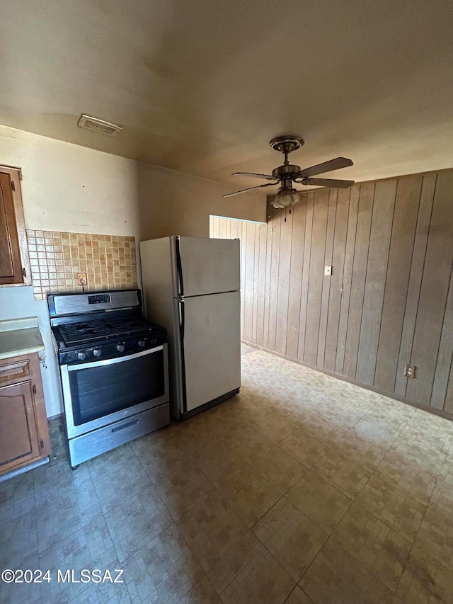 kitchen featuring stainless steel range with gas stovetop, wooden walls, ceiling fan, and white refrigerator