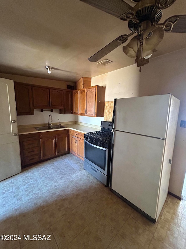 kitchen with white refrigerator, sink, stainless steel gas stove, and ceiling fan