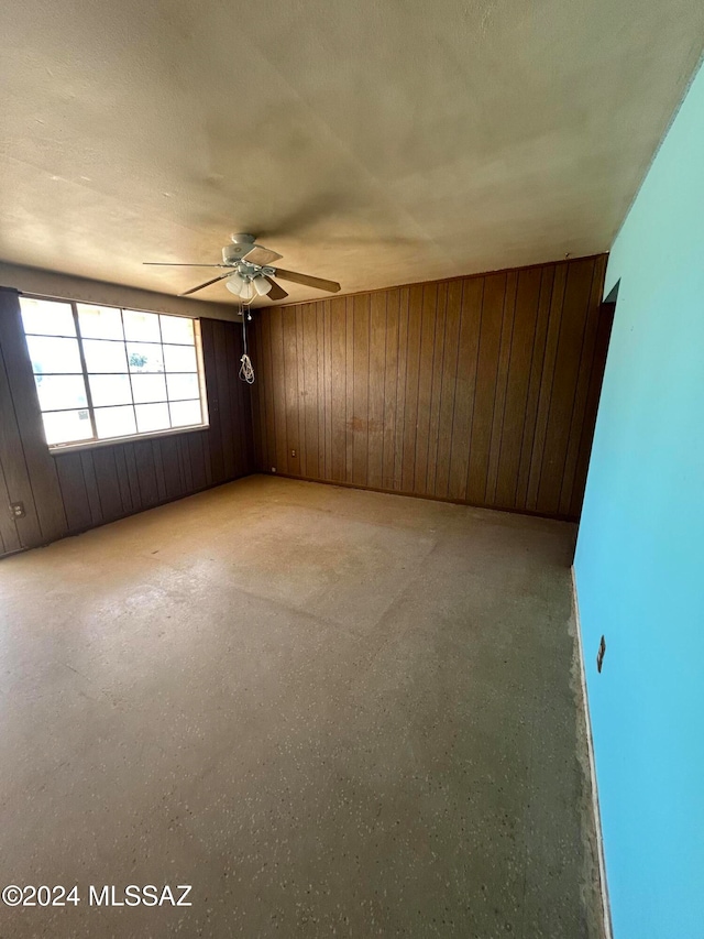 unfurnished room with wood walls, ceiling fan, and a textured ceiling