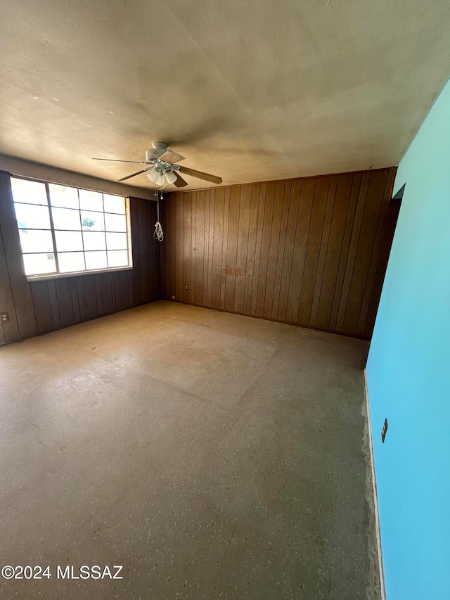 spare room featuring wood walls, a textured ceiling, and ceiling fan