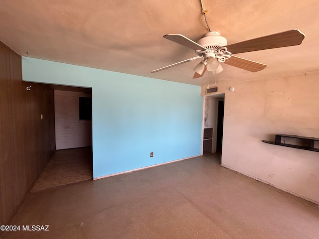 empty room featuring wood walls, concrete flooring, ceiling fan, and a textured ceiling