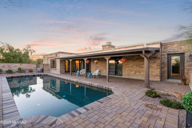 pool at dusk with a patio area