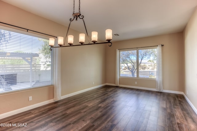 spare room featuring a wealth of natural light, dark wood-type flooring, and a chandelier