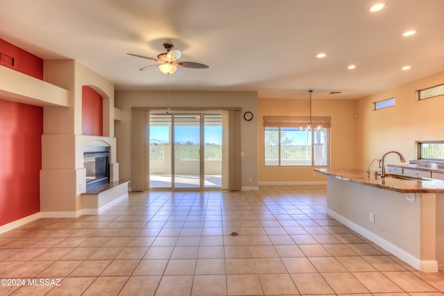 interior space featuring light stone countertops, sink, light tile patterned flooring, ceiling fan with notable chandelier, and hanging light fixtures