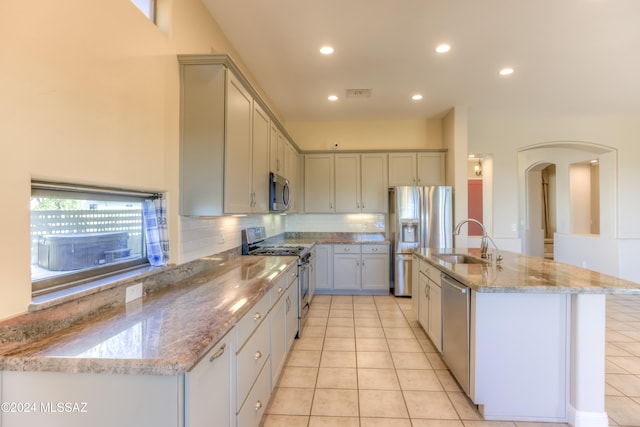 kitchen with appliances with stainless steel finishes, sink, light stone counters, and an island with sink