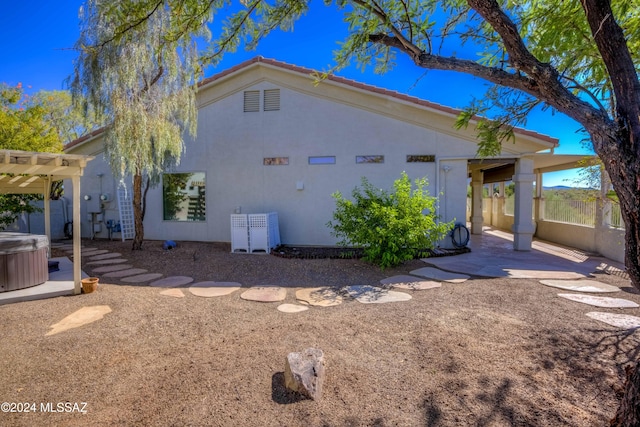 view of home's exterior with a hot tub, a patio area, and a pergola