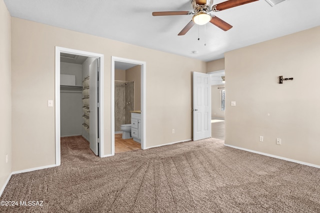 unfurnished bedroom featuring a spacious closet, a closet, light carpet, ceiling fan, and connected bathroom