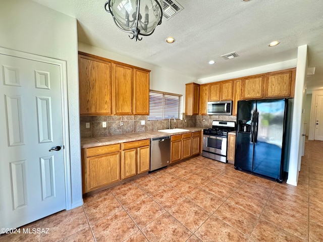 kitchen featuring tasteful backsplash, light tile patterned floors, sink, a notable chandelier, and stainless steel appliances