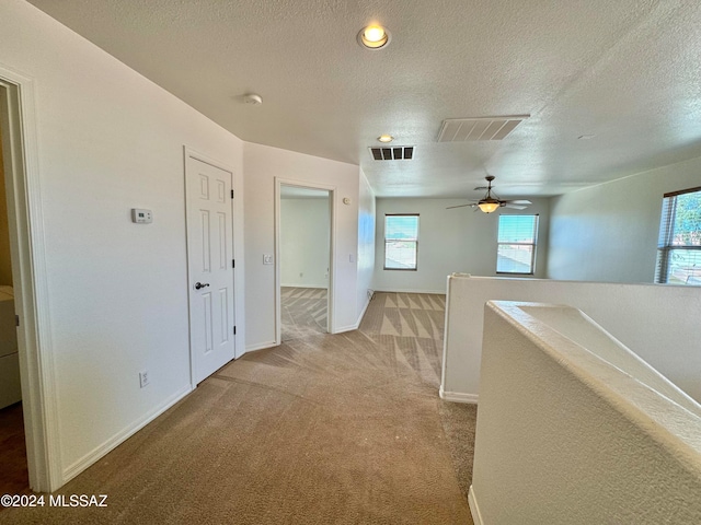 hall featuring a textured ceiling, carpet flooring, and a healthy amount of sunlight