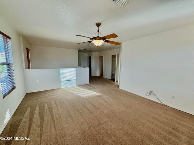 carpeted empty room with a textured ceiling, ceiling fan, and a wealth of natural light