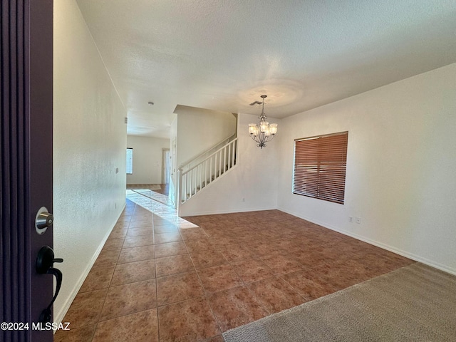 empty room with carpet flooring, a textured ceiling, and a chandelier