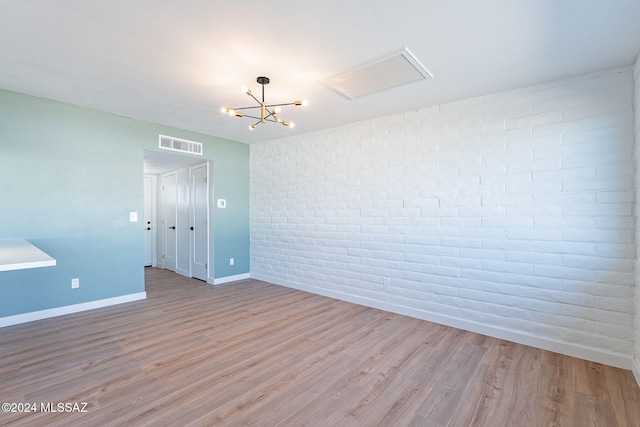 unfurnished room featuring light hardwood / wood-style floors, an inviting chandelier, and brick wall