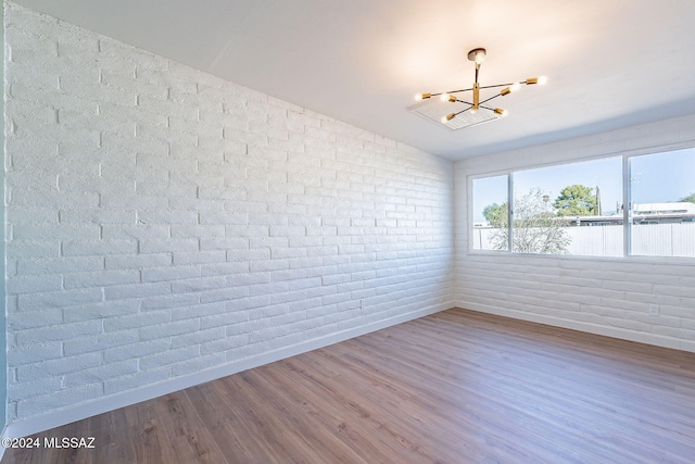 spare room featuring brick wall, hardwood / wood-style floors, vaulted ceiling, and a notable chandelier