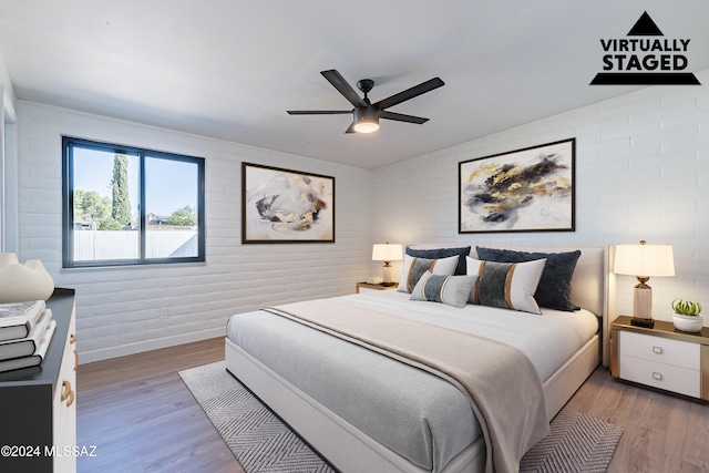 bedroom featuring brick wall, light hardwood / wood-style floors, and ceiling fan