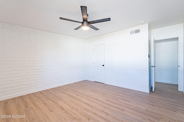 empty room with light hardwood / wood-style floors, brick wall, and ceiling fan