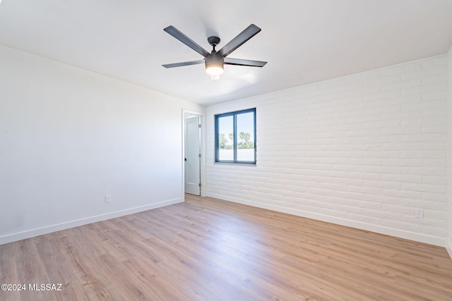 unfurnished room featuring brick wall, light wood-type flooring, and ceiling fan