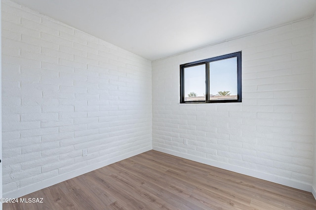 empty room featuring brick wall and hardwood / wood-style flooring