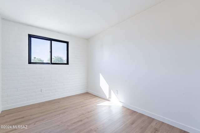 spare room featuring light hardwood / wood-style flooring and brick wall