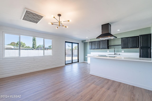 kitchen featuring a chandelier, light hardwood / wood-style flooring, wall chimney exhaust hood, sink, and brick wall