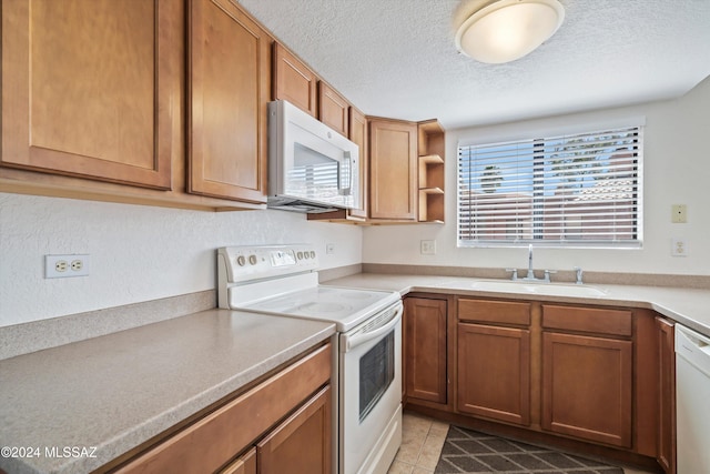 kitchen with a textured ceiling, sink, light tile patterned flooring, and white appliances