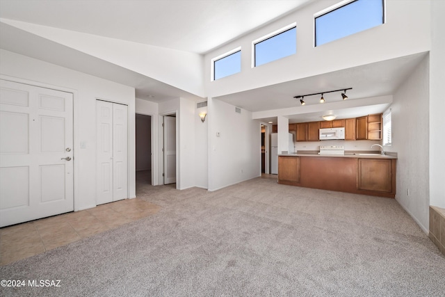 unfurnished living room featuring a high ceiling, light tile patterned floors, rail lighting, and light colored carpet