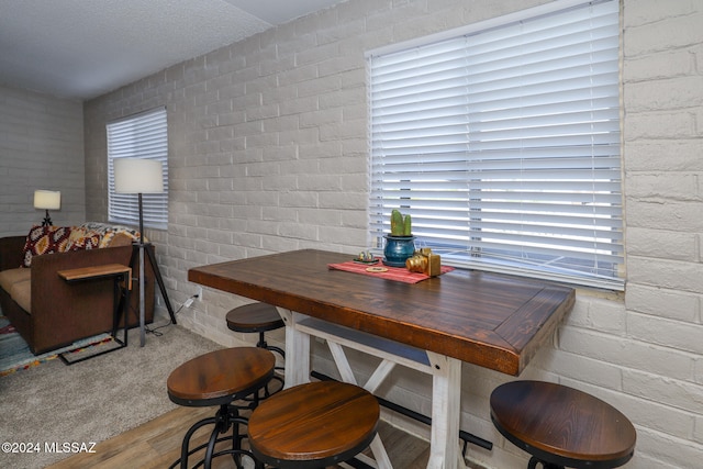 dining space with a healthy amount of sunlight, hardwood / wood-style flooring, a textured ceiling, and brick wall