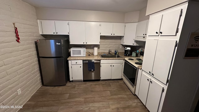 kitchen featuring sink, white cabinetry, stainless steel appliances, brick wall, and exhaust hood