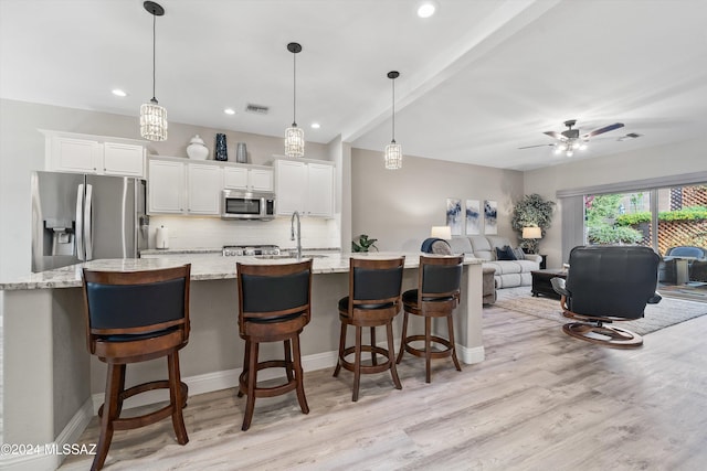 kitchen featuring white cabinetry, light stone counters, stainless steel appliances, and decorative light fixtures