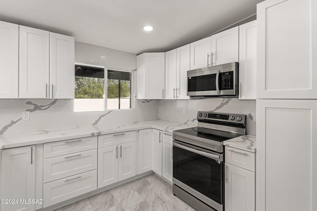 kitchen with appliances with stainless steel finishes, white cabinets, light stone countertops, and tasteful backsplash