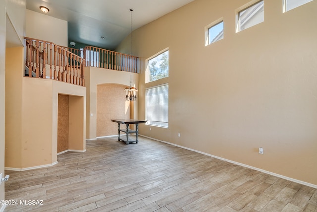 unfurnished living room featuring light hardwood / wood-style floors, a towering ceiling, and a chandelier