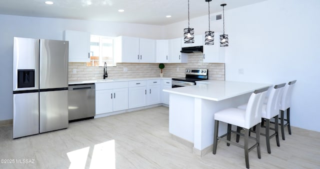 kitchen with a breakfast bar, appliances with stainless steel finishes, white cabinetry, hanging light fixtures, and kitchen peninsula