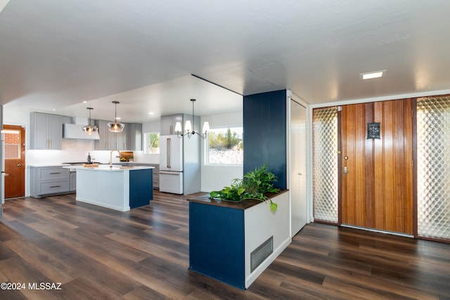 kitchen with white fridge, dark hardwood / wood-style flooring, an island with sink, and hanging light fixtures