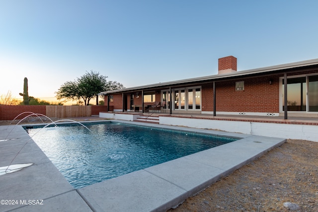 pool at dusk with pool water feature and a patio area