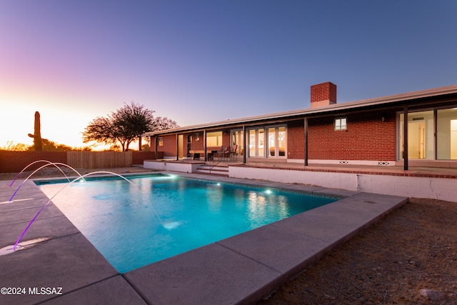 pool at dusk featuring pool water feature and a patio