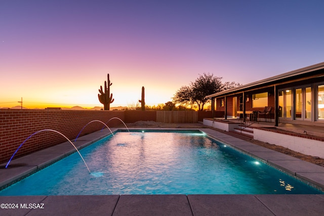 pool at dusk with pool water feature and a patio